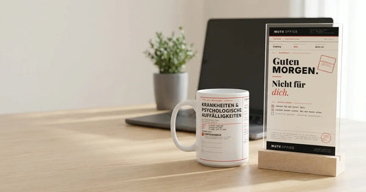 MUTE OFFICE – Einstands-Set: Coffeinismus-Tasse und Acryl-Aufsteller „Guten Morgen · Nicht für dich“ auf einem Schreibtisch am ersten Arbeitstag